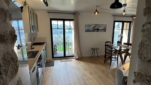 A spacious kitchen with a large window, a dining area with a table and chairs, and a view of the city. - Port & sea view - Elegant apartment for 2 in Audierne - L'Oasis sur mer (PLOUHINEC)