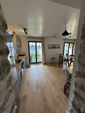 A spacious kitchen with a large window, a dining area with a table and chairs, and a view of the city. - Port & sea view - Elegant apartment for 2 in Audierne - L'Oasis sur mer (PLOUHINEC)
