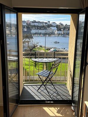 Ein Balkon mit Tisch und Stühlen, der auf ein Gewässer mit Booten und Gebäuden im Hintergrund blickt.