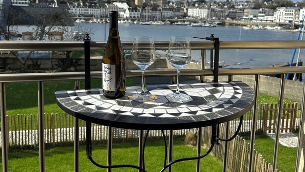 A table with a bottle and glasses, overlooking a harbor with buildings and a clear sky. - Port & sea view - Elegant apartment for 2 in Audierne - L'Oasis sur mer (PLOUHINEC)