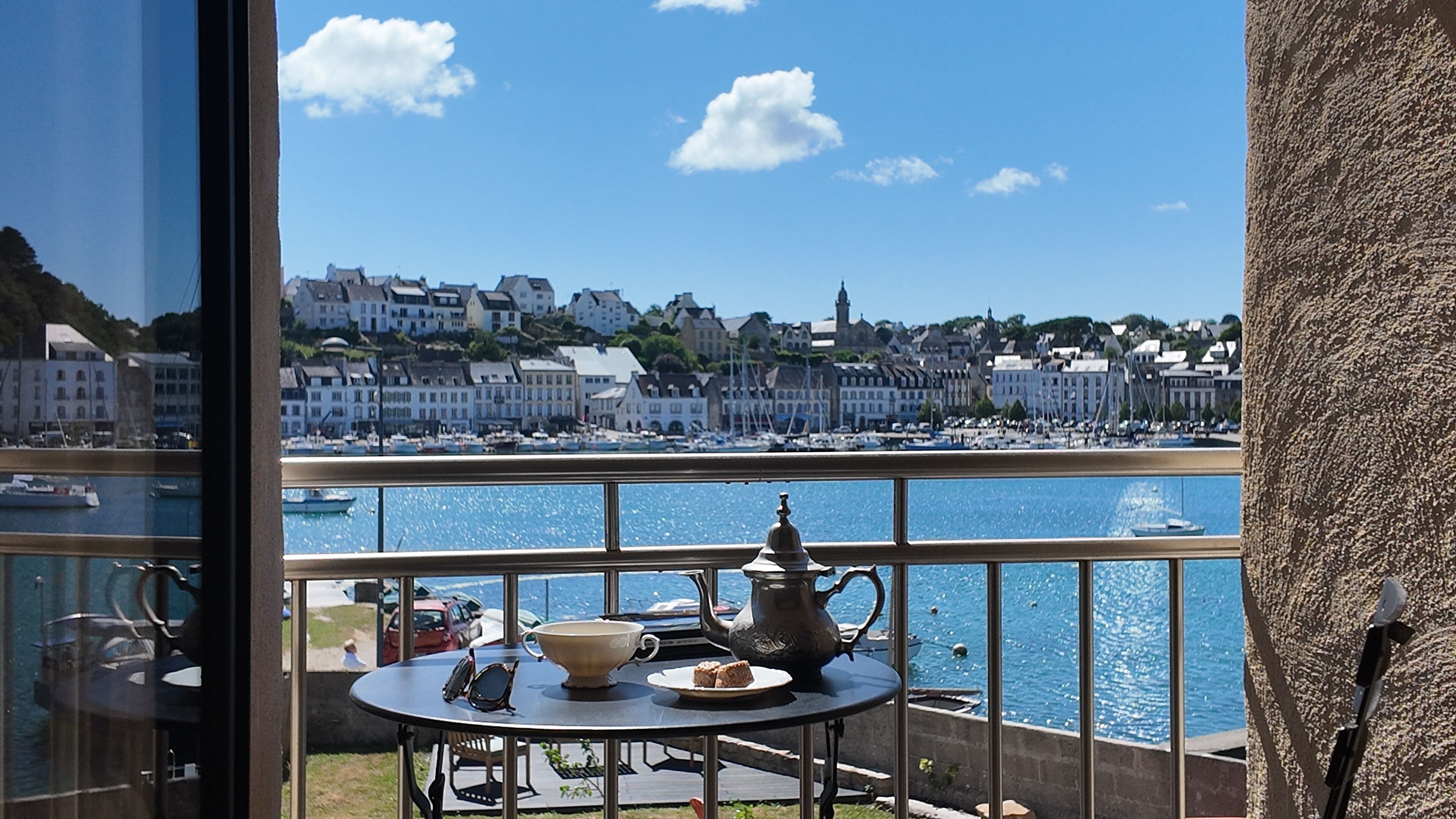 A balcony with a table set for tea, overlooking a harbor with boats and buildings.