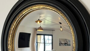 A round mirror with a gold frame reflecting a dining area with a table, chairs, and a hanging light fixture. - Port & sea view - Elegant apartment for 2 in Audierne - L'Oasis sur mer (PLOUHINEC)