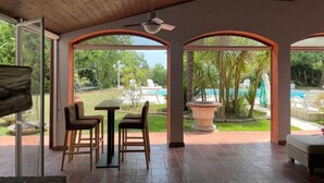 A covered patio with a pool view, wooden ceiling, and arched windows.