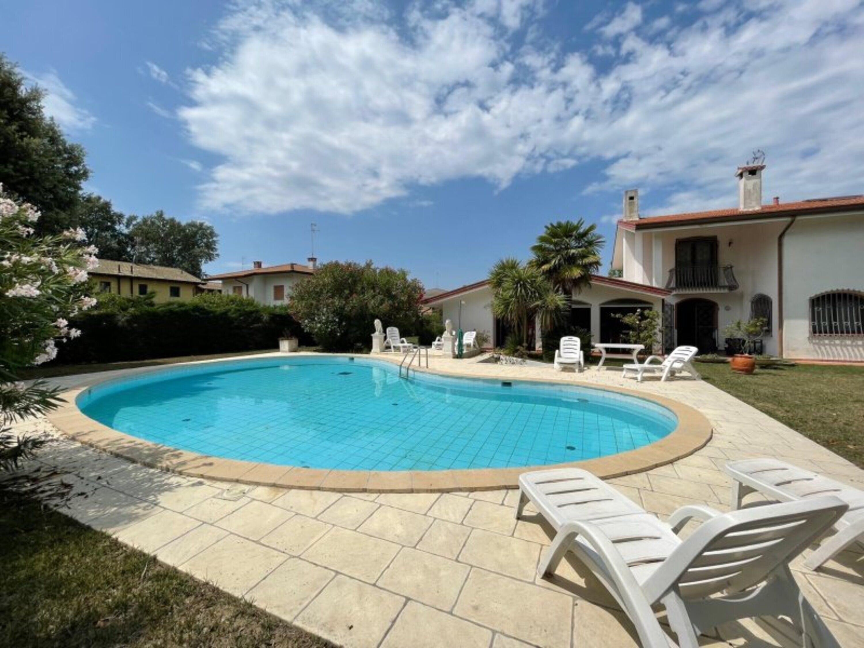 Une piscine avec des chaises longues, un espace patio et un bâtiment doté d’un toit en tuiles.