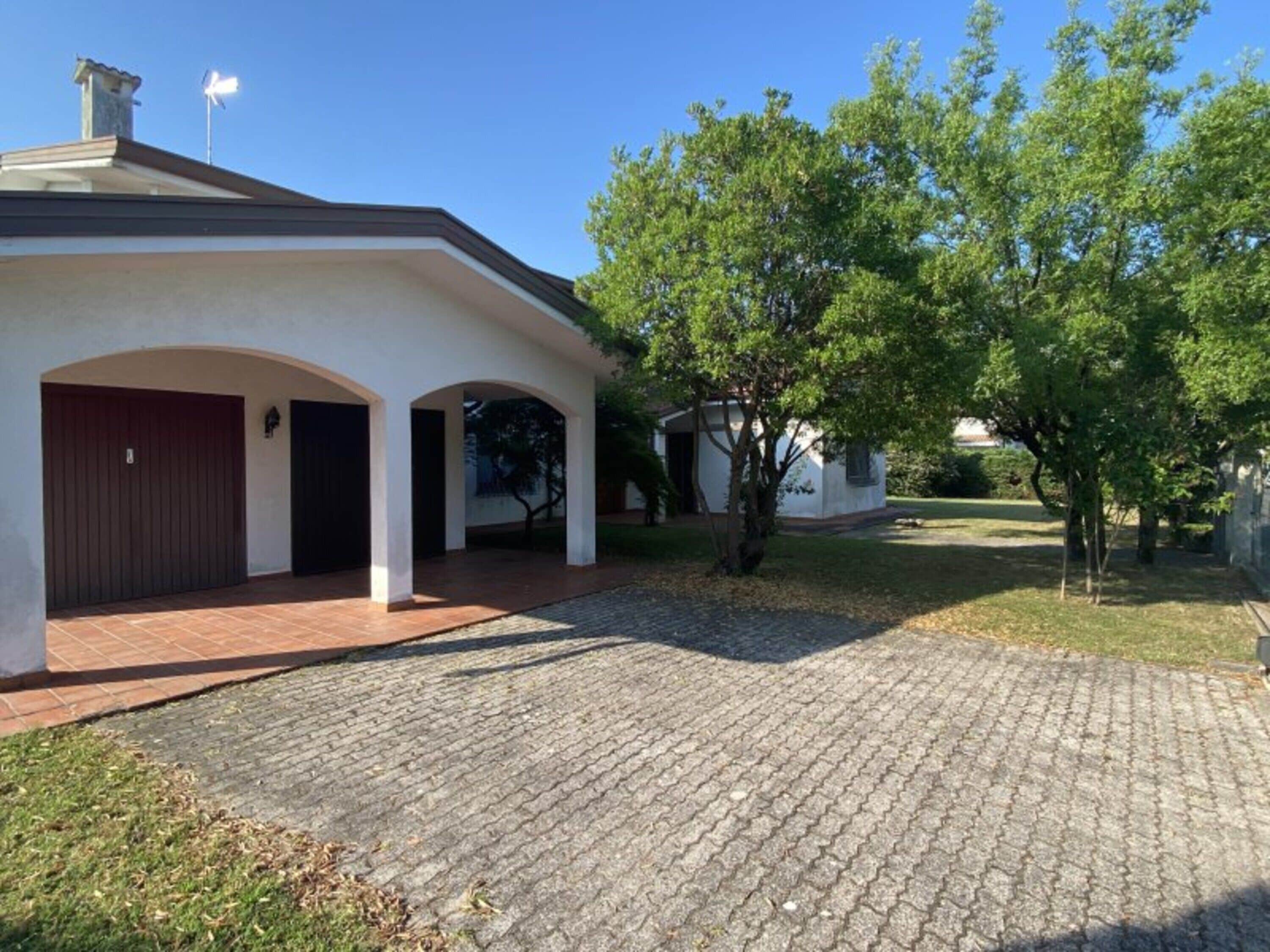 A building with a paved driveway, a covered entrance with arches, and a tree in the foreground.