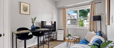 Un salon moderne avec un canapé, une table à manger et des chaises, un téléviseur et une fenêtre avec des rideaux.