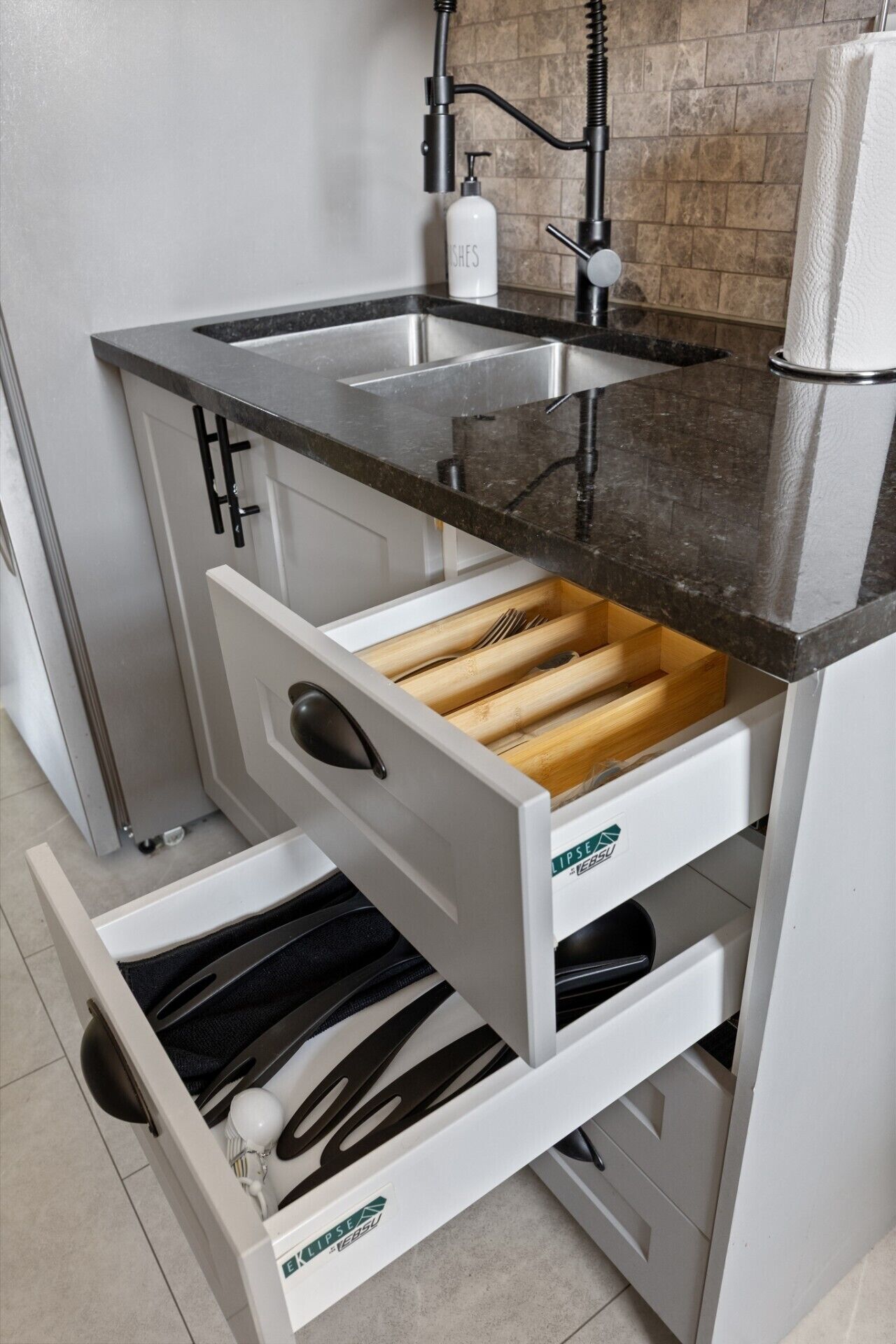 Een keuken met een roestvrijstalen spoelbak, een zwart aanrecht en witte kastjes.