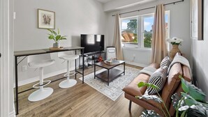 A modern living room with a sofa, coffee table, TV, and bar stools. - Stay Together but with  Privacy of Two Fully Equipped Apartments (Windsor)