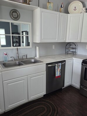 A kitchen with white cabinetry, a stainless steel sink, a dishwasher, and a stove.