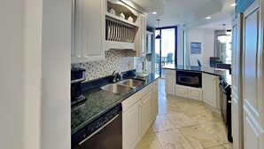 A modern kitchen with white cabinetry, a granite countertop, a dishwasher, and a view to the dining area. - Surfside #612 & 612a (Miramar Beach)