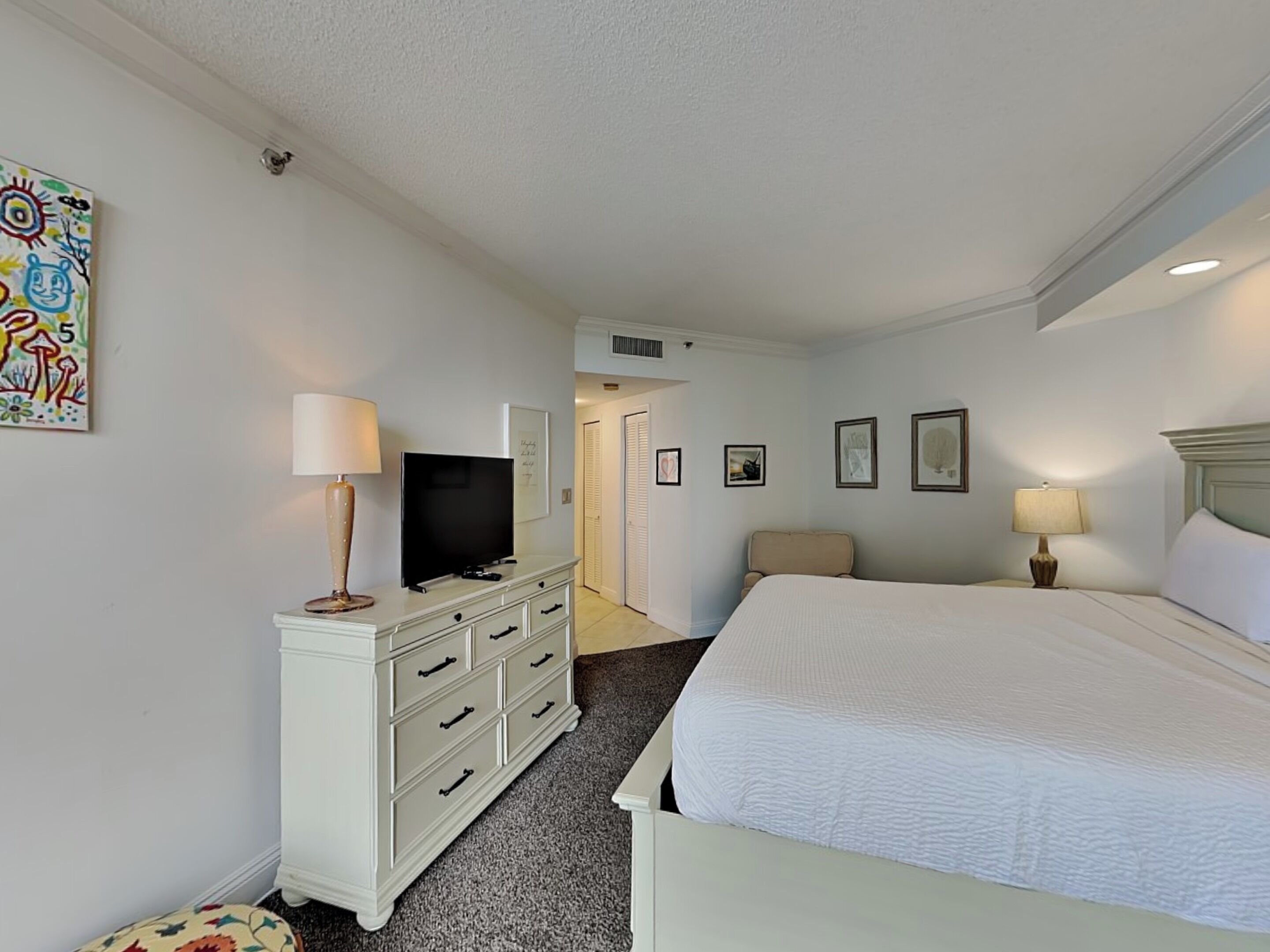A hotel room with a bed, a TV on a dresser, a chair, and a door leading to another room.