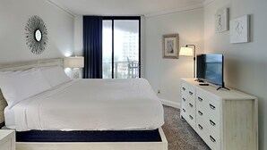 A hotel room with a bed, a TV, a dresser, a mirror, and a window with curtains. - Surfside #612 & 612a (Miramar Beach)
