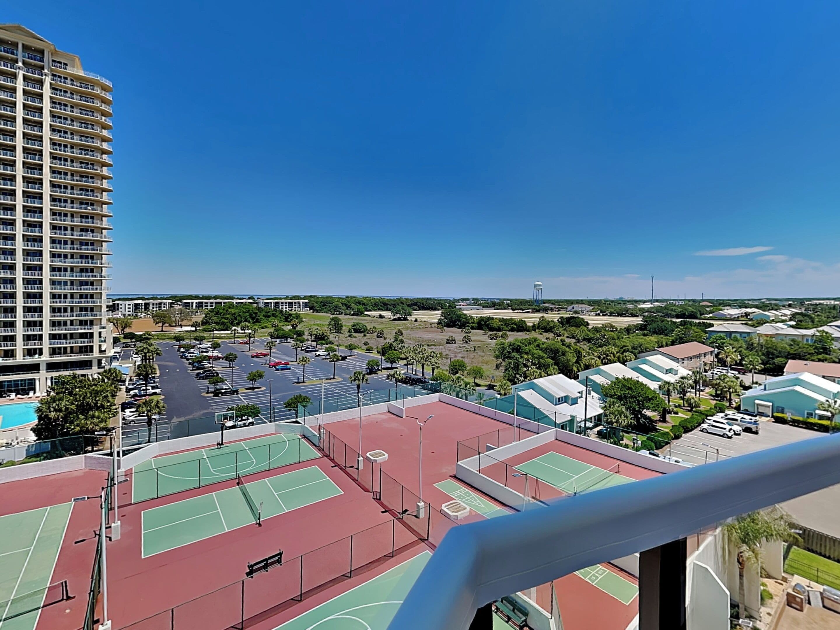 A high-rise hotel with multiple floors, a tennis court complex, and a clear view of the surrounding area.