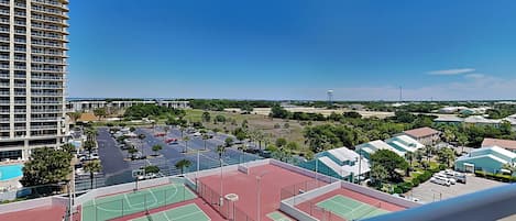 A high-rise hotel with multiple floors, a tennis court complex, and a clear view of the surrounding area.