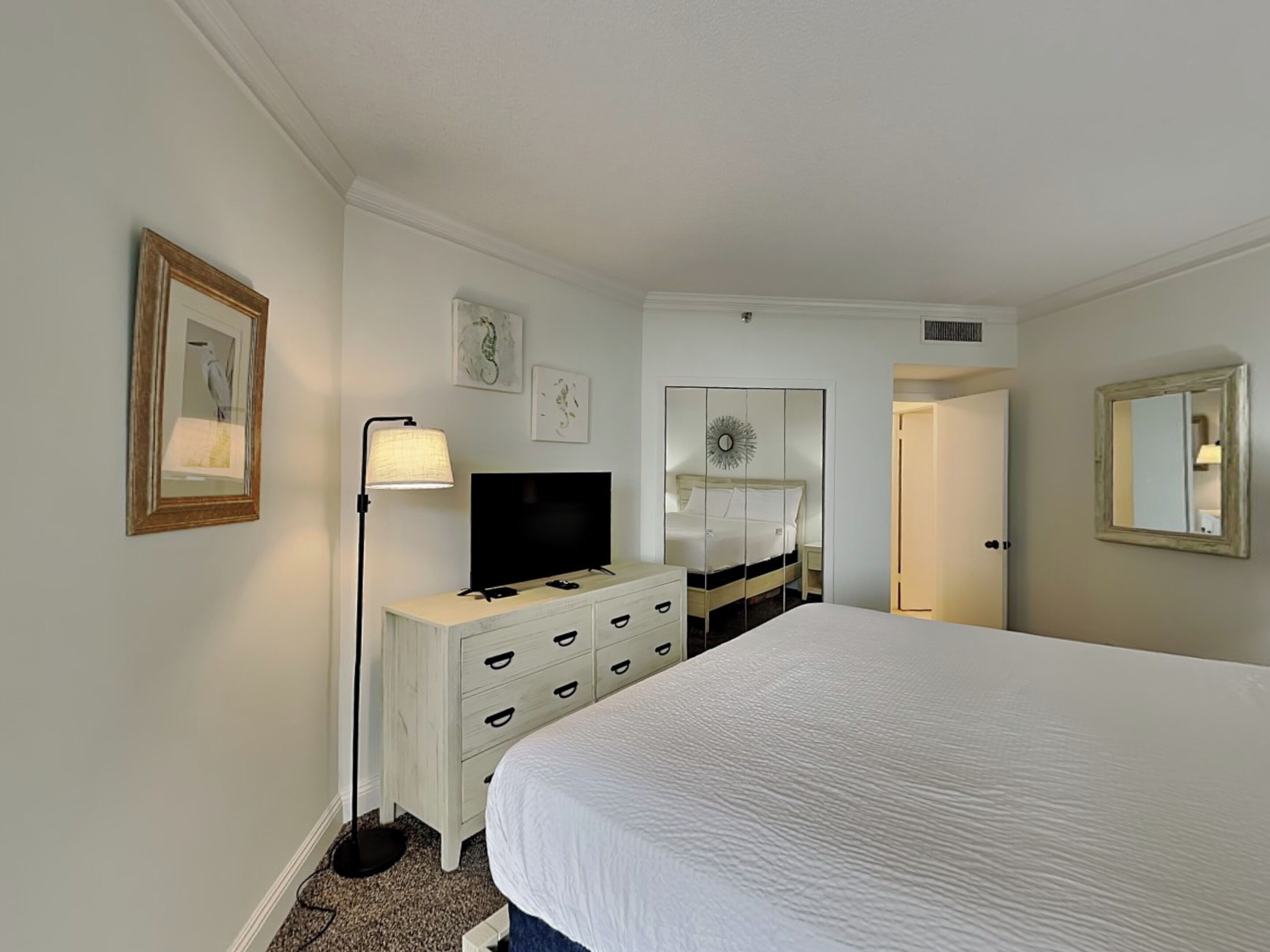 Ein Hotelzimmer mit Bett, Schminktisch, Fernseher, Spiegel und Bildern an den Wänden.