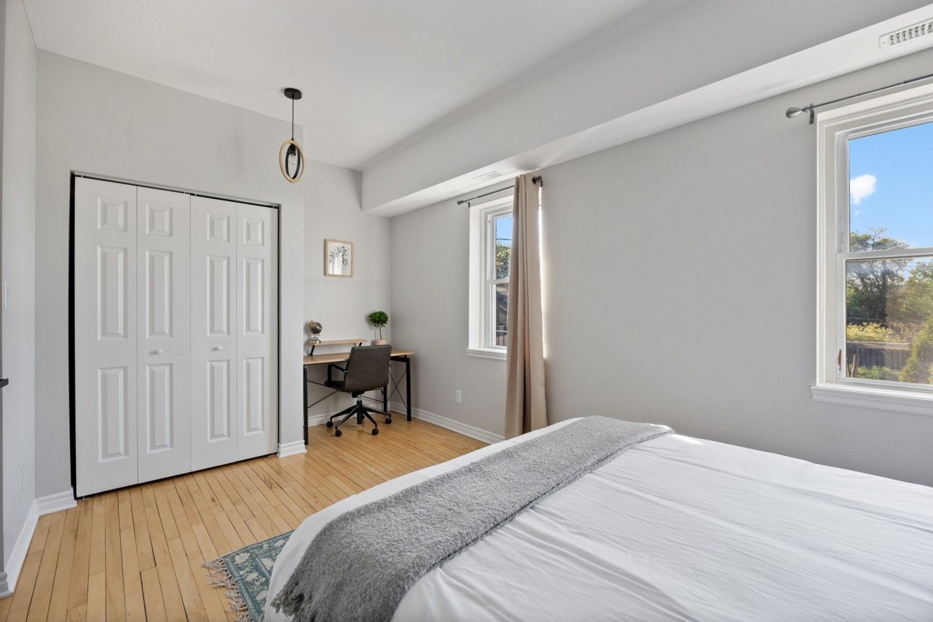A bedroom with a bed, a desk, a chair, a door, and a window.