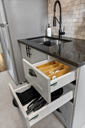 A kitchen with a black countertop, a sink, and a drawer with utensils.