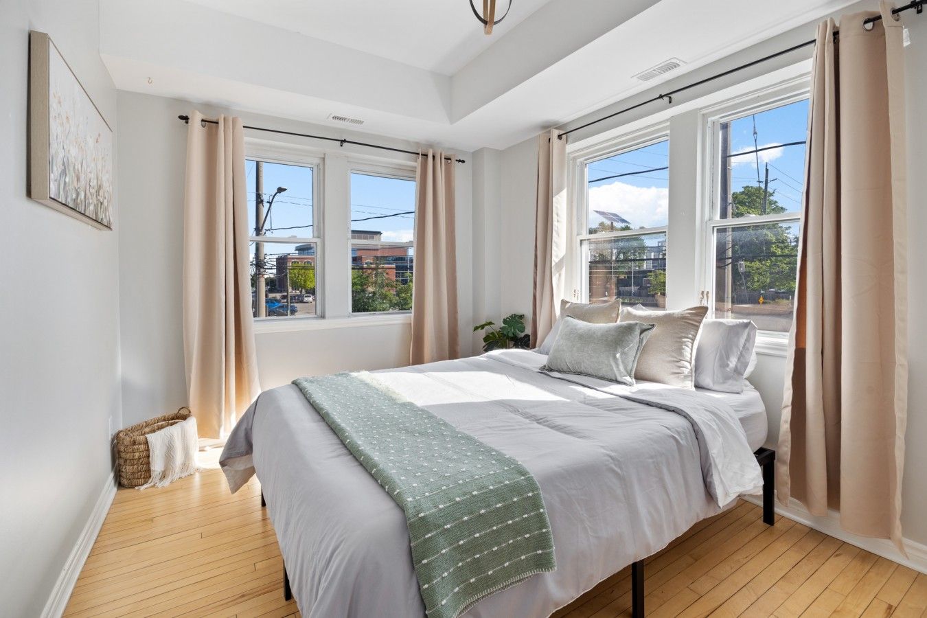 A bedroom with a large bed, two windows, and a view of buildings outside.