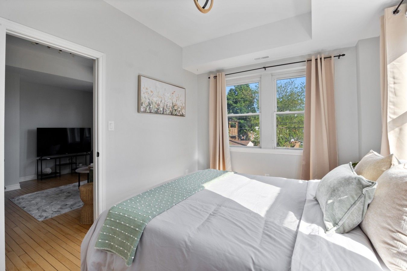 Um quarto com uma cama, televisão, janela com cortinas e um quadro na parede.