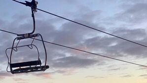 Eine Sesselbahn schwebt über einer verschneiten Berglandschaft bei klar blauem Himmel.