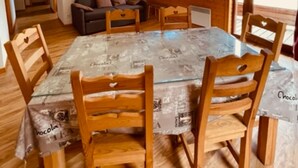 Ein Essbereich mit einem großen Tisch, Holzstühlen und einer Couch im Hintergrund.