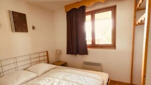Ein Schlafzimmer mit einem hölzernen Bettgestell, einem Nachttisch, einem Fenster mit Vorhängen und einem an der Wand hängenden Bild.