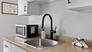 Een keuken met een roestvrijstalen spoelbak, een zwarte kraan, een magnetron en een lijst aan de muur.