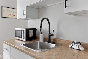 A kitchen with a stainless steel sink, a black faucet, a microwave, and a framed sign on the wall. - Walkerville Windsor | 3BR | 2 Private Apartments | Sleeps 6 (Windsor)