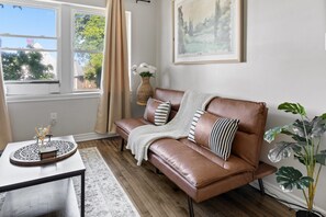 A brown leather sofa with striped pillows, a woven basket with white flowers, and a large plant. - Walkerville Windsor | 3BR | 2 Private Apartments | Sleeps 6 (Windsor)