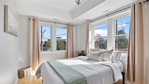 Een slaapkamer met een groot bed, twee ramen en uitzicht op gebouwen.