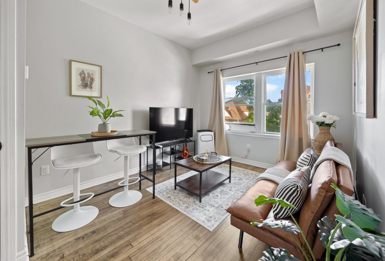 Uma sala de estar moderna com sofá, mesa de centro, TV e banquetas de bar.