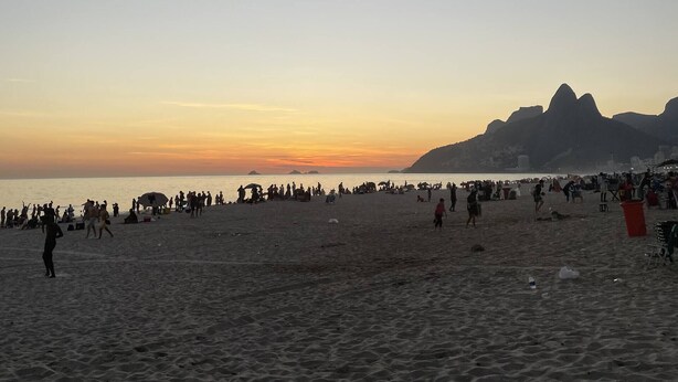 Une plage avec des gens, une montagne et un coucher de soleil.