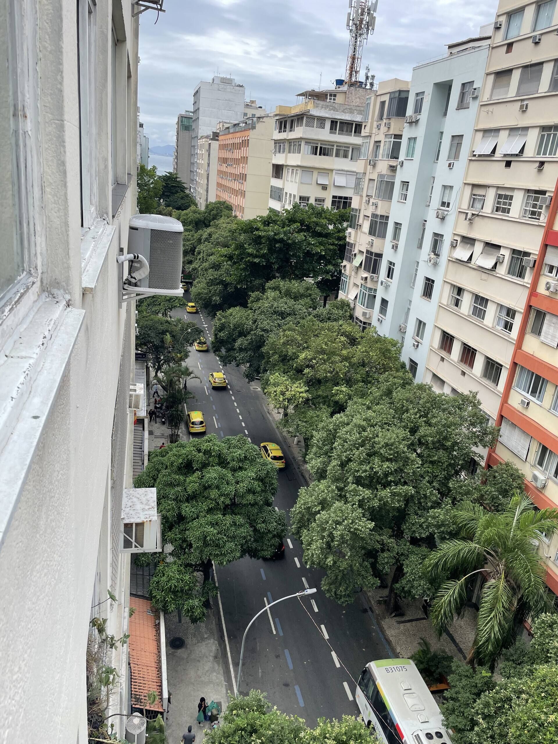 A multi-story building with balconies, a street with yellow taxis, and dense greenery.