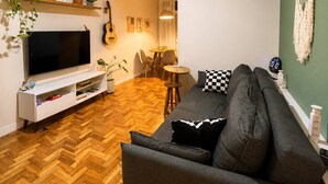 Un salon équipé d’un téléviseur, d’un canapé, d’un plancher en bois, d’un ventilateur de plafond et d’un coin repas.