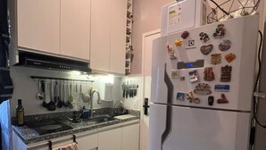 Une cuisine de taille réduite, avec des meubles blancs, un réfrigérateur en acier inoxydable et une cuisinière à gaz.