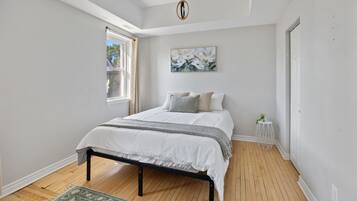 A bedroom with a bed, a window, a painting, and a small white table.