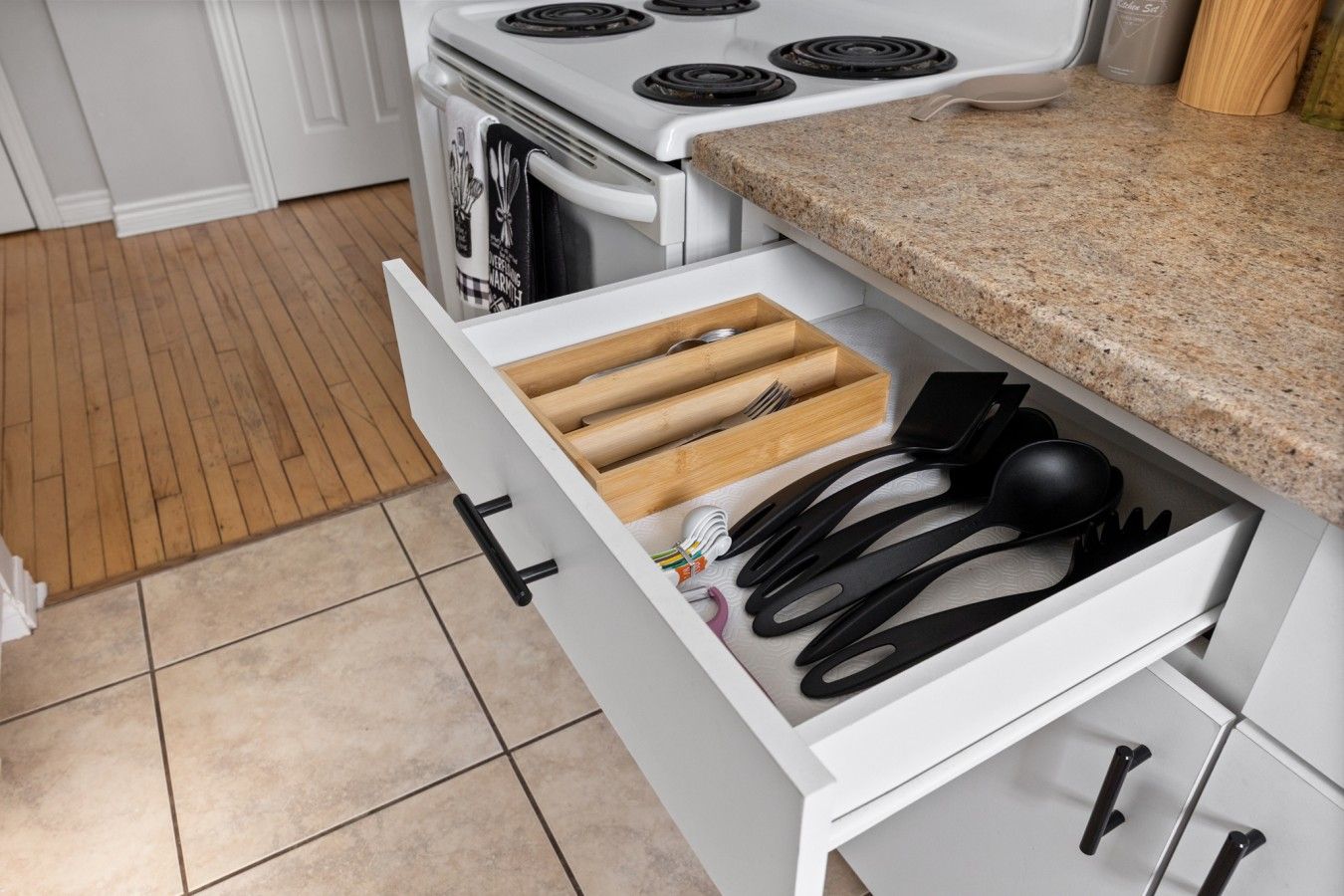 A kitchen with a white stove, a drawer with wooden utensils, and a granite countertop.