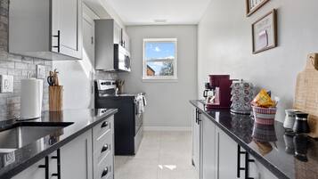 A modern kitchen with a black stove, white cabinets, and a window with a view.