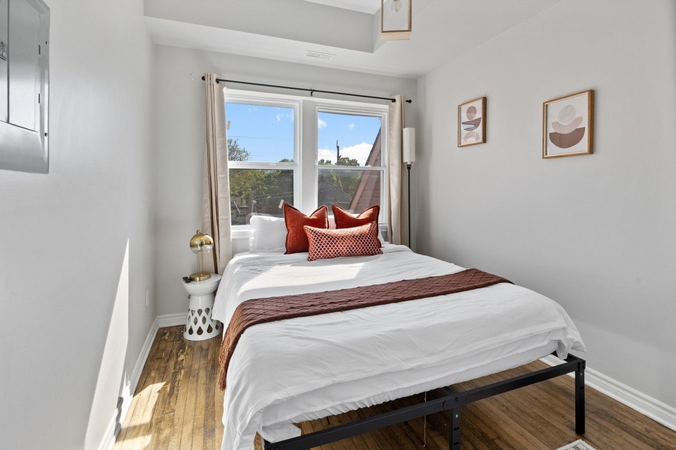 A bedroom with a bed, a window, a bedside table, and two framed pictures on the wall.
