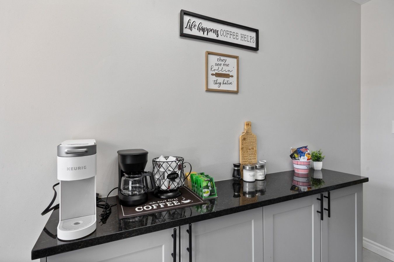 A kitchen counter with a Keurig coffee maker, a coffee grinder, and a coffee-themed sign.