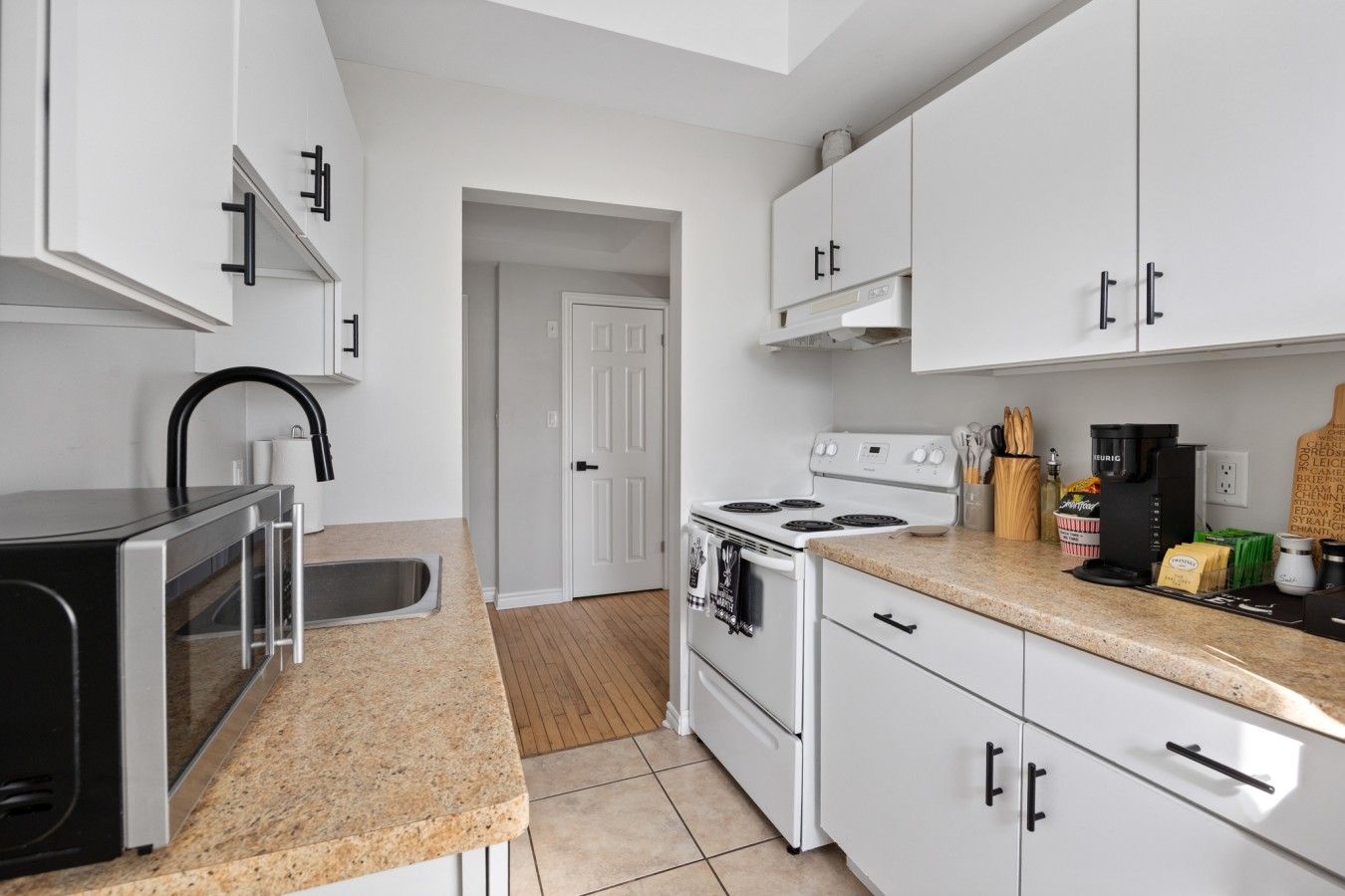 A compact kitchen with white cabinets, a stainless steel sink, a stove, and a coffee maker.