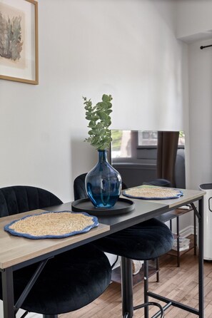 Uma área de refeições moderna com uma mesa de madeira, cadeiras pretas, um vaso azul com plantas verdes e um jogo americano trançado.