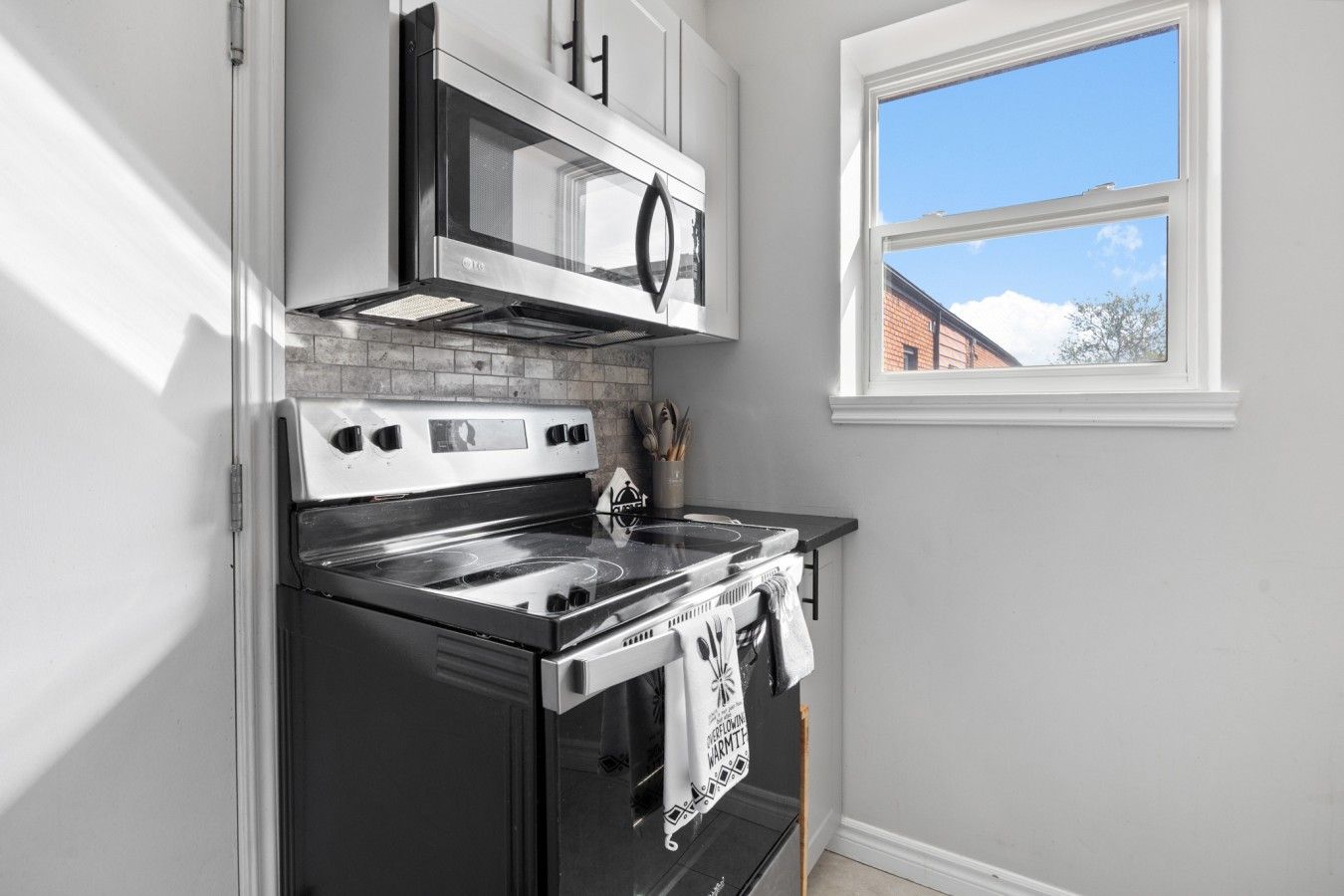 A kitchen with a stove, microwave, and oven, a window with a view, and a tiled backsplash.