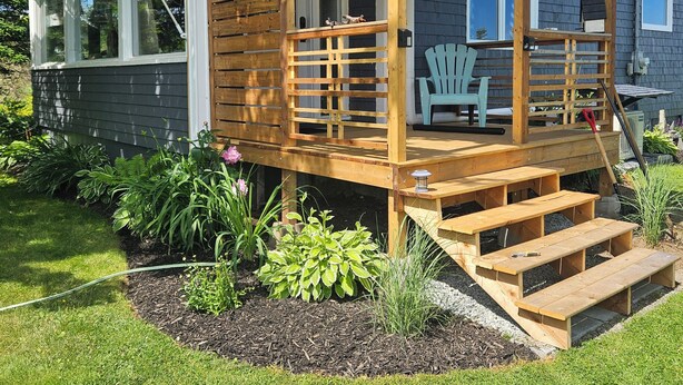 A wooden deck with a bench and a table, surrounded by a garden with various plants.