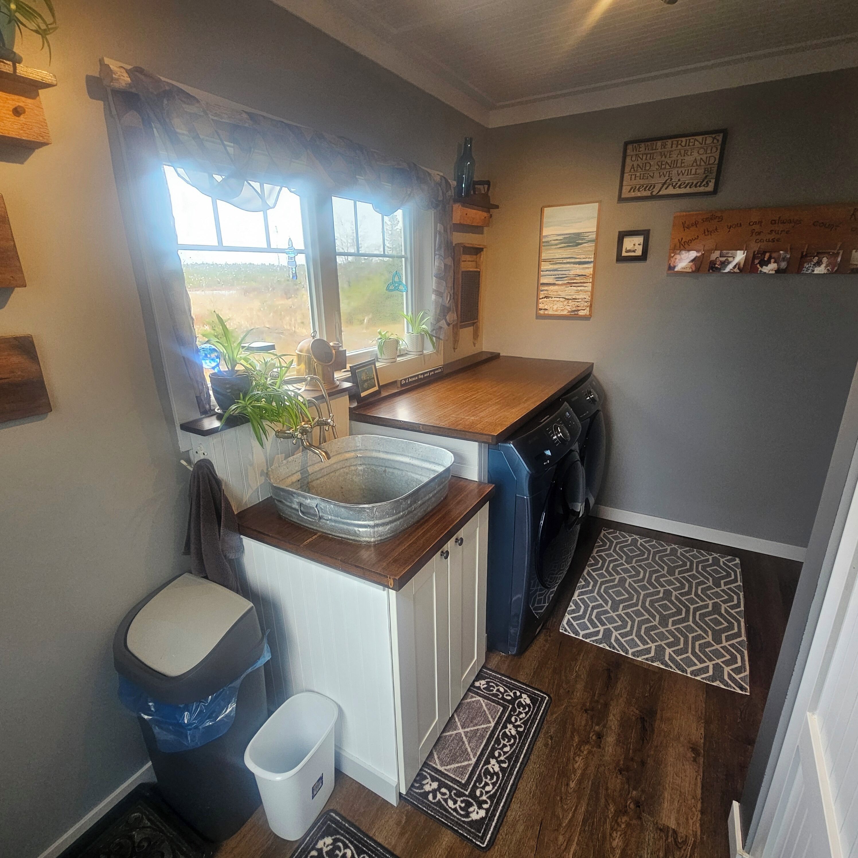 A compact kitchen with a sink, a washing machine, and a window with curtains.