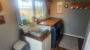 Una cocina compacta con lavamanos, lavadora y ventana con cortinas.