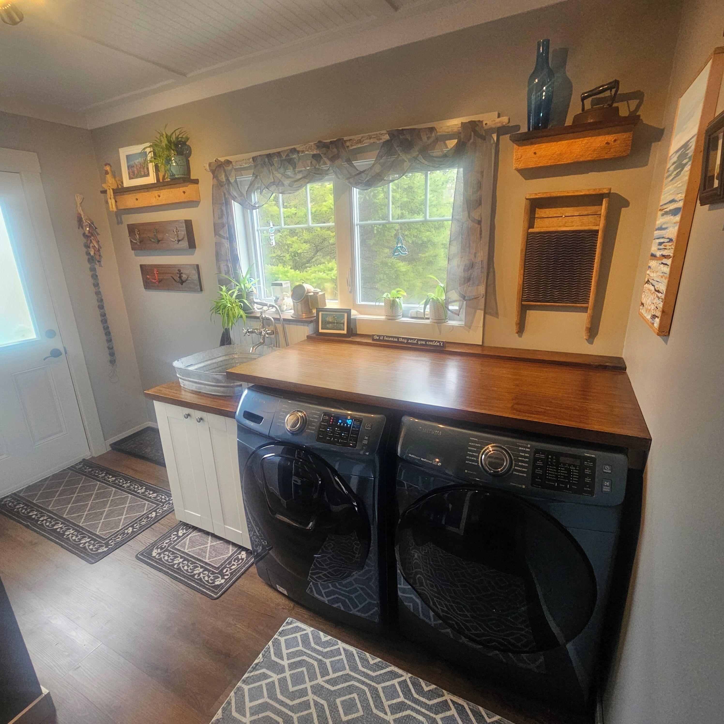A compact kitchen with a washing machine, a sink, and a window with curtains.