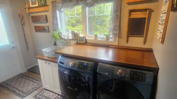 A compact kitchen with a washing machine, a sink, and a window with curtains.