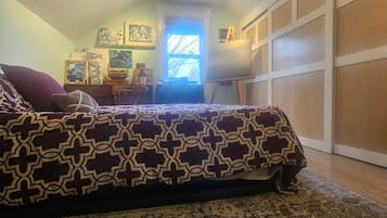 A bedroom with a patterned bedspread, a desk with a lamp, a window with natural light, and a garage door.