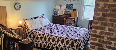 A bedroom with a bed, a desk, a chair, a clock, and artwork on the walls.